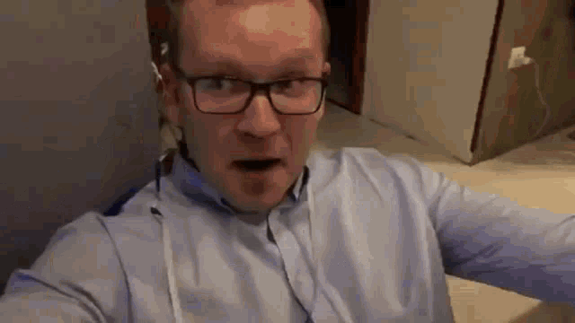 a man wearing glasses and a blue shirt is making a surprised face .
