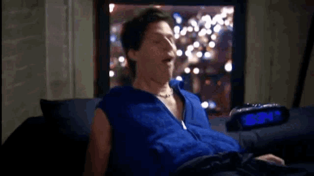 a man is laying on a couch with his eyes closed and an alarm clock behind him .