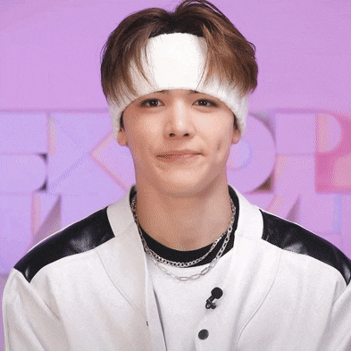 a young man wearing a white headband and a necklace looks at the camera