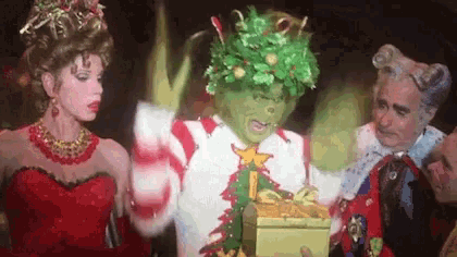 the grinch is wearing a christmas wreath on his head and holding a gift .
