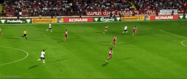 soccer players on a field with ads for konami and carlsberg on the sidelines