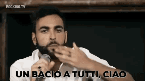 a man with a beard is holding a microphone in his hand and saying un bacio a tutti ciao .