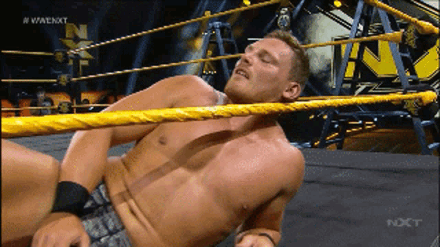 a shirtless wrestler is laying in a wrestling ring with the word nxt on the screen
