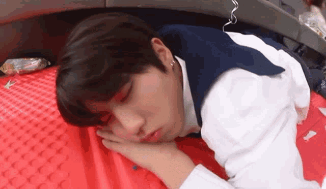a young man is sleeping on a red blanket on the floor .