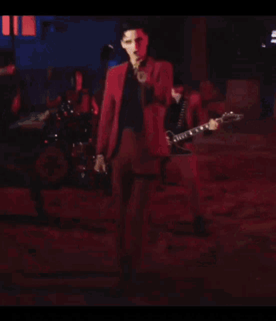 a man in a red suit is playing a guitar in a band