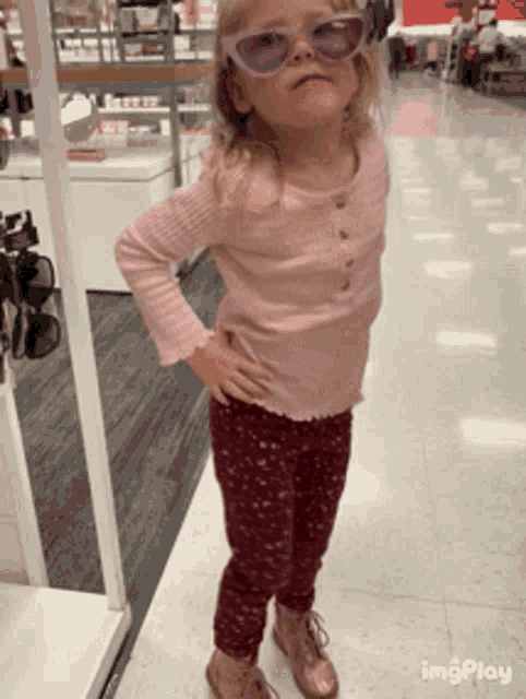a little girl wearing sunglasses stands with her hands on her hips in a store ..