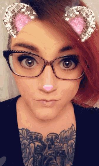 a woman wearing glasses has a pink nose and a tattoo on her chest