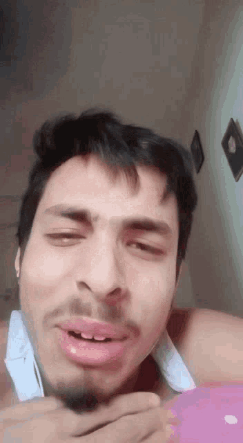 a man with a beard and a white tank top is making a funny face