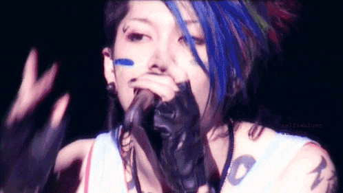 a woman with blue hair and a tattoo on her arm is singing into a microphone ..