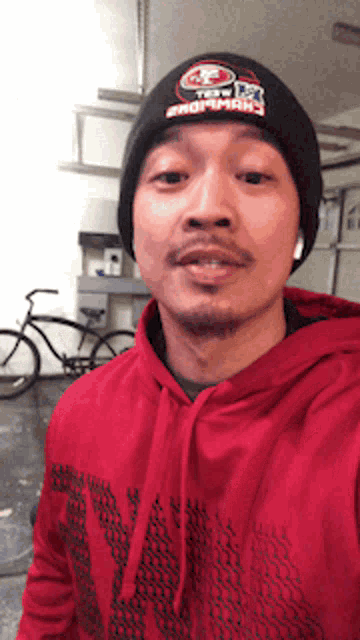 a man wearing a red hoodie and a black beanie with the word san francisco written on it