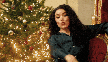 a woman sitting in front of a christmas tree making a face