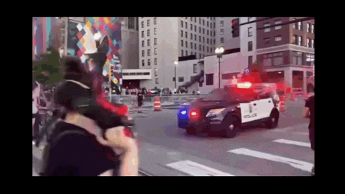 a police car is driving down a city street with a crowd behind it .