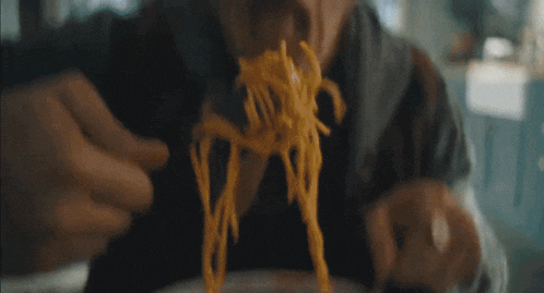 a man is eating noodles with a fork and spoon .