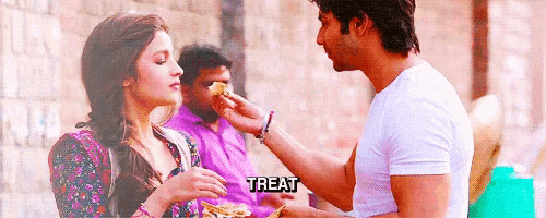 a man is feeding a woman a piece of food and the word treat is on the bottom of the image .