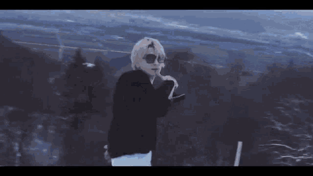 a man wearing sunglasses is standing on top of a mountain .