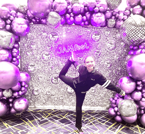 a girl stands in front of a wall with purple balloons and a sign that says jamfest on it