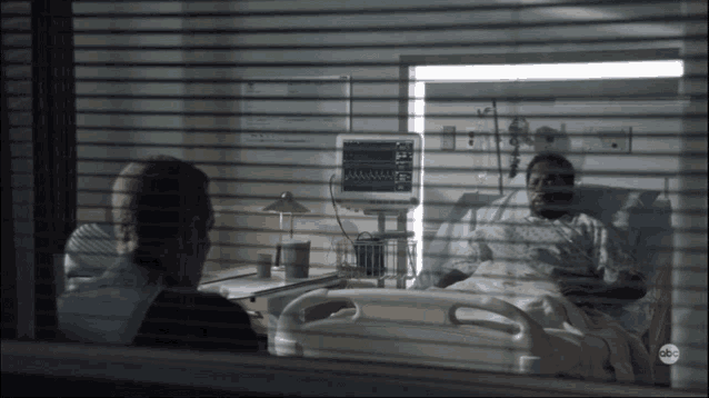 a man sits in a hospital room talking to a patient