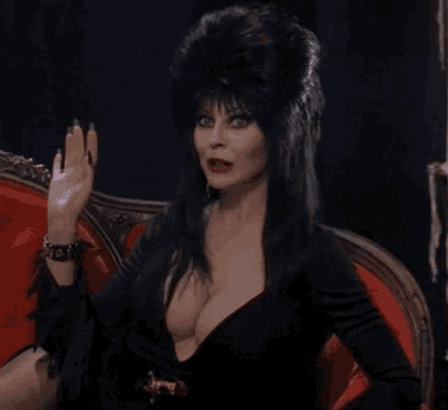 a woman in a black dress and hat is sitting on a red couch .