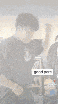 a man in a black shirt is standing in a room with a sign that says `` good perc '' .