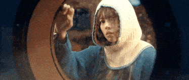a woman in a blue sweater with a white hood is looking through a window