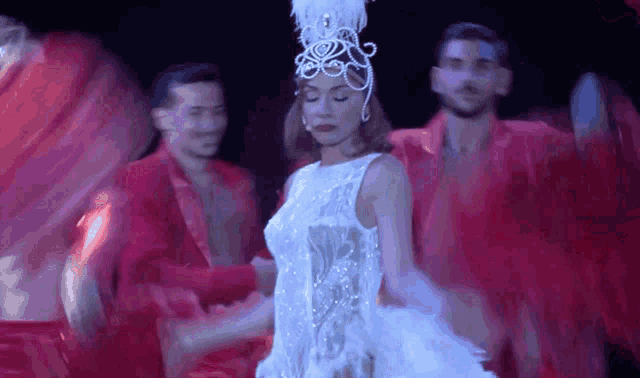 a woman in a white dress and feathered headpiece is dancing on a stage