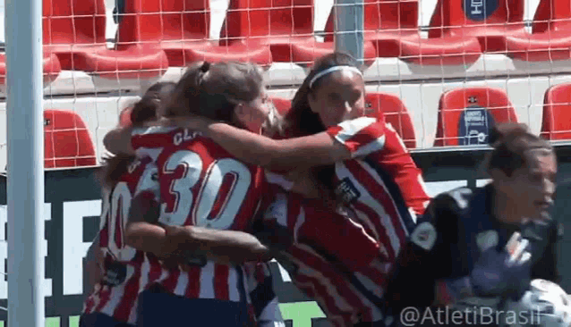 a group of women are hugging each other on a soccer field . one of the players has the number 30 on her jersey .