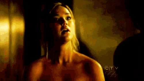 a naked woman is standing next to a man in a dark room and looking at the camera .