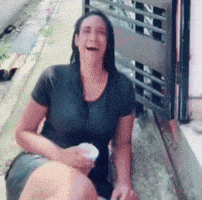 a woman in a black shirt is sitting on a sidewalk holding a cup and smiling