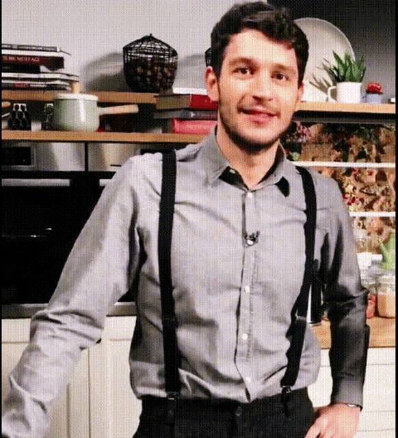 a man wearing suspenders and a gray shirt is standing in a kitchen