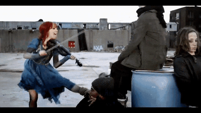 a woman in a blue dress is playing a violin while a man sits on a blue drum