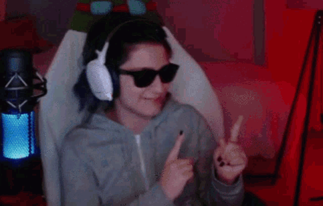 a woman wearing headphones and sunglasses is giving a thumbs up sign while sitting in a chair .