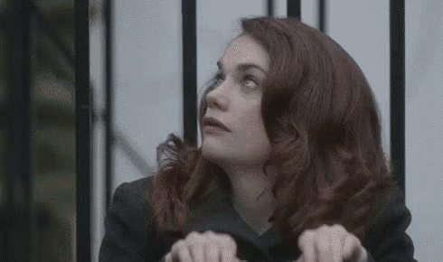 a woman with red hair is making a funny face with her hands while standing in front of a fence .