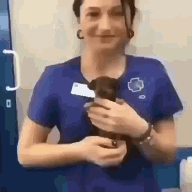 a woman in a blue shirt is holding a small dog in her arms .