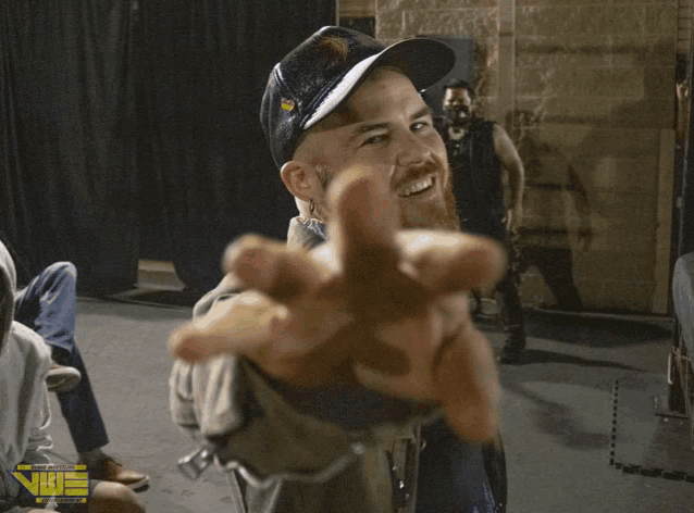 a man wearing a hat that says ' nbt ' on it reaches out his hand