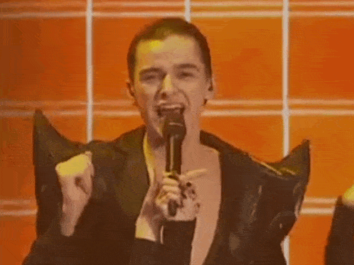 a man is holding a microphone and singing into it while wearing a black jacket .