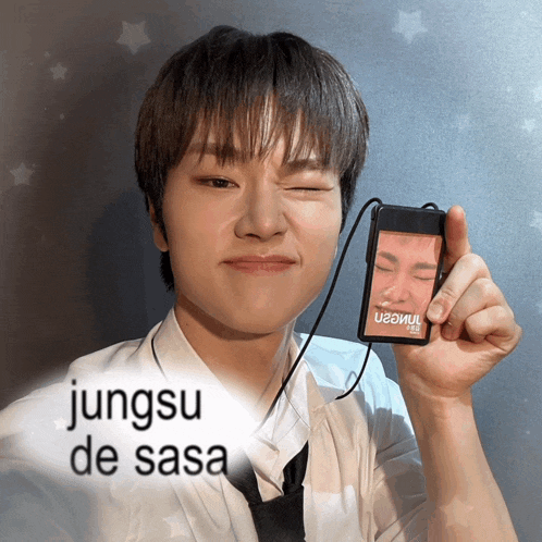 a young man is holding a phone with a picture of his face on it and the words jungsu de sasa above him