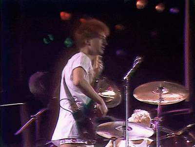 a man in a white shirt is playing drums in front of a microphone