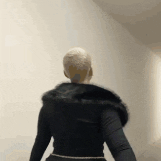 a woman wearing a black fur coat is standing in front of a wall .