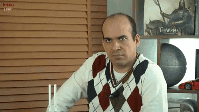 a man wearing a plaid sweater is sitting in front of a shelf that says tekno seyir on it
