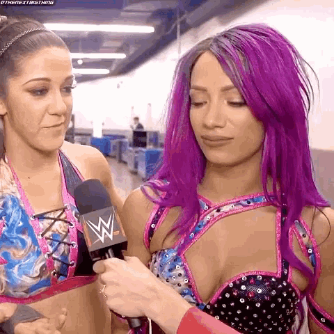 a woman with purple hair is talking into a microphone while another woman looks on .