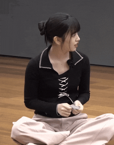 a woman wearing a black lace up top is sitting on the floor