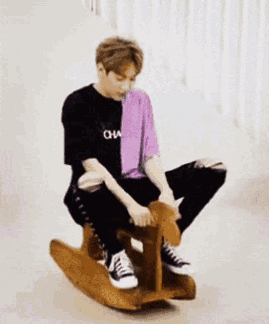 a young man is sitting on a wooden rocking horse with his hands in the air .
