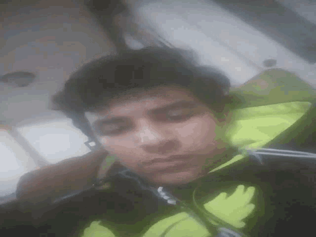 a young man wearing a black and yellow jacket is taking a selfie with his eyes closed .