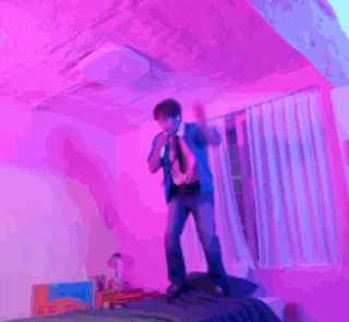 a person kneeling on a bed in a room with purple lights