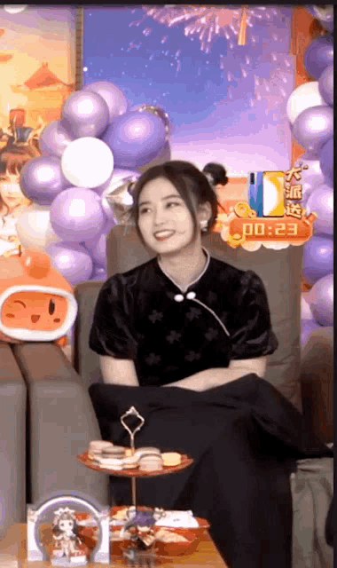 a woman is sitting in front of balloons and a sign that says 00 :23