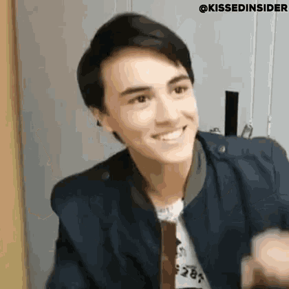 a young man in a blue jacket and tie is smiling and making a funny face .