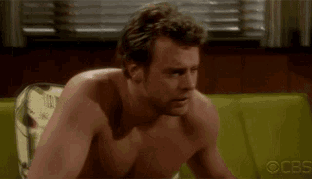 a shirtless man is sitting on a couch in a living room .