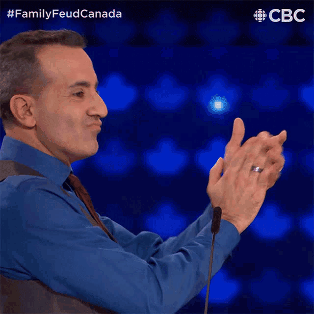 a man applauds in front of a microphone with the words familyfeud canada above him