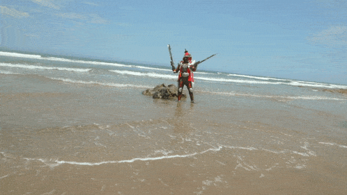 a person in a robot costume holding two swords on a beach