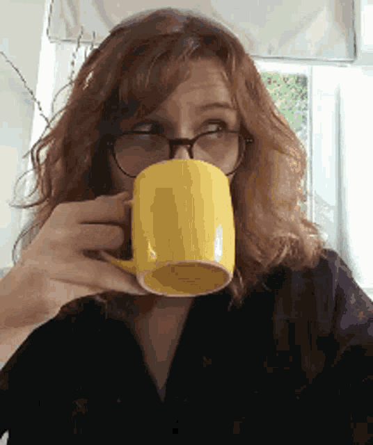 a woman with glasses is drinking from a yellow cup